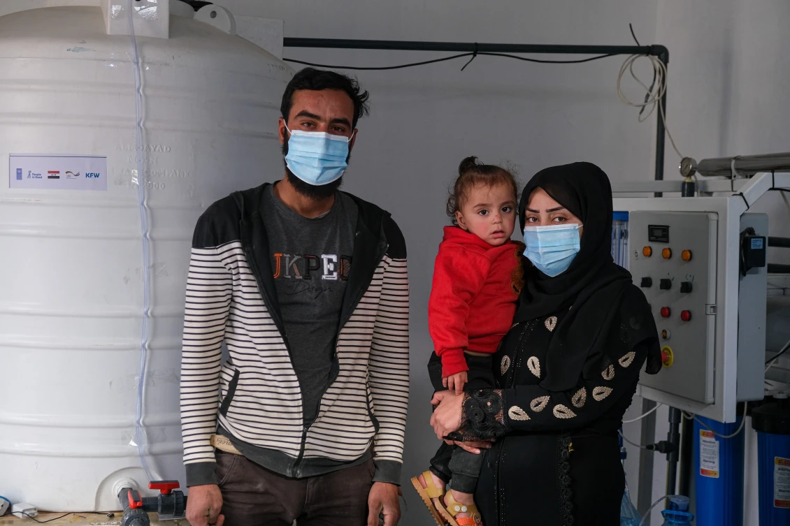 Athir and his wife Aline posing to the camera, with their 2-year-old daughter, in their drinking water purification project in Beiji, Iraq.
